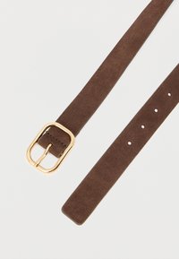 Hnedý semišový opasok so zlatou kovovou prackou, s plochým dizajnom a niekoľkými nastavovacími dierkami po celej dĺžke. Mäkká textúra.