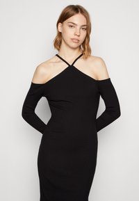 Vestido de malha canelada preto com design ombro a ombro, mangas longas e detalhe de tiras cruzadas no decote. Textura suave.