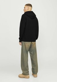 Sweatshirt à capuche noire avec des manches longues, associé à un pantalon baggy vert clair. L'ensemble présente un tissu texturé et des variations tonales subtiles.