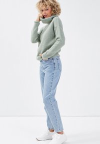 Suéter de cuello alto verde claro con puños y dobladillo acanalados; combinado con pantalones vaqueros de cintura alta de mezclilla azul clara; zapatillas deportivas blancas.