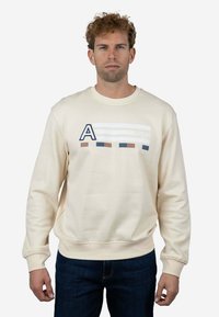Sudadera color crema hecha de algodón, con un gráfico que presenta un logo con la letra 'A' y franjas horizontales en azul, marrón y blanco. Puños y dobladillo acanalados.