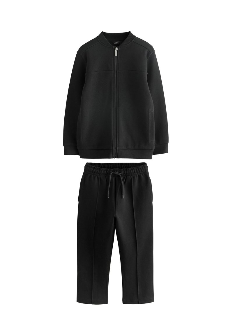 Sudadera negra con cremallera, cuello acanalado y dos bolsillos frontales, combinada con pantalones jogger negros de cintura elástica. Textura suave.