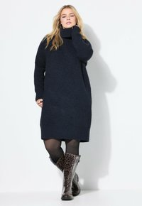 Vestito oversize in maglina blu navy con colletto alto e orlo a coste, abbinato a stivali leopardati al ginocchio e collant neri.