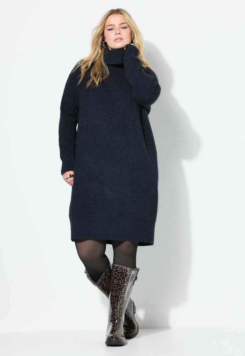 Vestito oversize in maglina blu navy con colletto alto e orlo a coste, abbinato a stivali leopardati al ginocchio e collant neri.