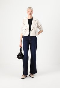 Cropped white leather biker jacket, black t-shirt, flared dark denim jeans, beige shoes, and a black patterned handbag.