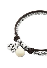 Pulsera de cuero con cuentas de plata; cuenta con un amuleto en relieve y una cuenta lisa de color marfil. En conjunto, una combinación de texturas y acabados.