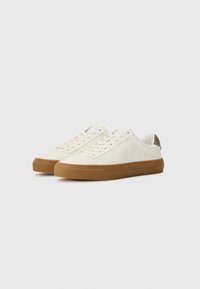 White sneakers with a smooth leather upper, rubber gum sole, round toe, and lace closure. Subtle branding on the side and heel accents.