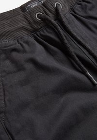 Schwarze Jogginghosen mit elastischem Bund und verstellbarem Kordelzug, die eine glatte Textur und minimalistische Nähdetails aufweisen.