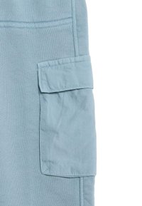 Ljusblå cargo-byxor har en texturerad tyg med en synlig patch-ficka på sidan, som visar sömnadsdetaljer och släta kanter.