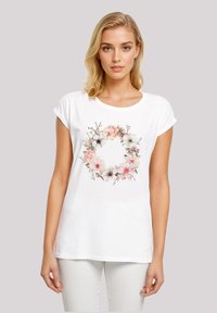 White cotton t-shirt featuring a floral wreath design in soft pinks and greens, with rolled short sleeves and a round neckline.