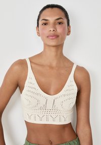 Bralette de punto crema con un escote en V profundo, que presenta un diseño texturizado y una banda acanalada en la parte inferior. Las tirantes son delgadas y ajustables.