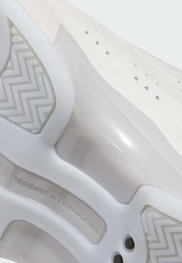 White sneaker with a textured surface, perforated detailing, and clear rubber sole. Features zigzag pattern on outsole and "DESIGNED IN LOS ANGELES" label.