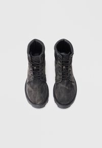 Botas negras con acabado texturizado, diseño con cordones, cuello acolchado y suela de goma resistente. Costuras y ojales visibles.