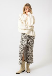 Sweatshirt oversized crème avec logo doré, associé à une jupe midi en imprimé léopard avec une fente sur le côté. Des bottes de cow-boy beiges complètent le look.