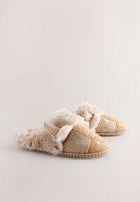 Chaussons doublés en fausse fourrure avec un design textile beige et marron, mettant en valeur des accents en chevrons et des oreilles décoratives. Semelle en daim avec détails de couture.