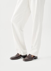 Καφέ δερμάτινα μοκασίνια με υφή και χαμηλό χοντρό τακούνι, σε συνδυασμό με άνετο λευκό παντελόνι.