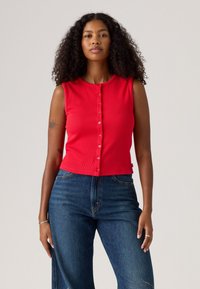 Débardeur rouge côtelé avec un col rond et une fermeture à boutons sur le devant, associé à un jean taille haute bleu foncé.