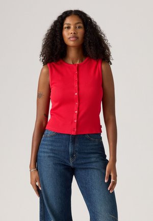 Top sem mangas vermelho com textura, decote redondo e fecho de botões na frente, combinado com jeans de denim azul de cintura alta.