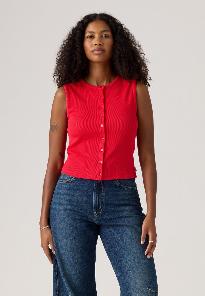 Débardeur rouge côtelé avec un col rond et une fermeture à boutons sur le devant, associé à un jean taille haute bleu foncé.