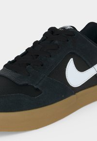 Μαύρο sneaker χαμηλού προφίλ με λευκό σχέδιο Nike, μαύρα κορδόνια και σόλα από καουτσούκ.