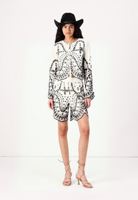 White outfit featuring intricate black embroidery, including a blouse with long sleeves and shorts with scalloped edges, complemented by a black hat.