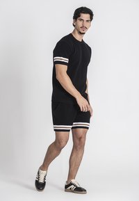 T-shirt nera a maglia con maniche a righe bianche e beige abbinata a pantaloni corti neri. Indossata con scarpe nere e crema.