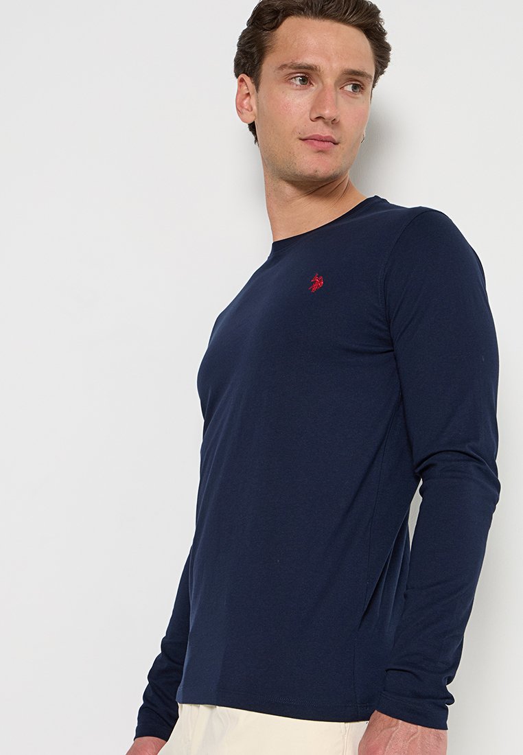 Marineblaues Langarm-T-Shirt aus leichtem Baumwollstoff. Mit einem kleinen roten Logo auf der Brust und einer taillierten, glatten Textur.