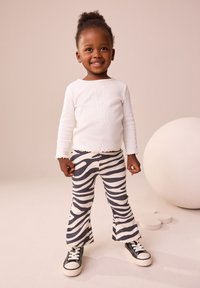 Hvid, ribbet langærmet top med frynser på kanterne, kombineret med vide bukser med zebra-striber i sort og creme, og sorte sneakers.