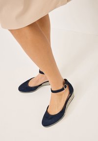 Námořnické modré semišové wedges boty mají pásek kolem kotníku s kovovou sponou a tkanou texturu na klínovém podpatku. Design s otevřenou špičkou.