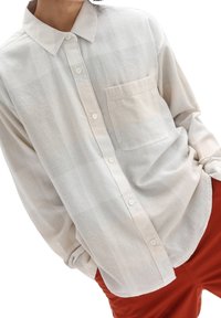 Camicia button-up beige chiaro realizzata in tessuto morbido e texture. Presenta una tasca frontale e un delicato motivo a quadretti. Vestibilità rilassata con maniche lunghe.