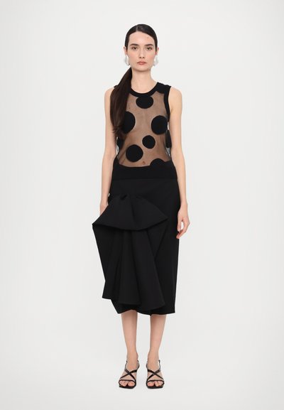 Black sleeveless top with sheer fabric and large black polka dots, paired with a sculptural black skirt featuring a prominent bow detail.