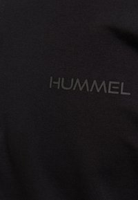 T-shirt nera realizzata in tessuto morbido, con un sottile logo "HUMMEL" in rilievo sulla parte frontale. Design semplice, senza ulteriori fantasie o dettagli.