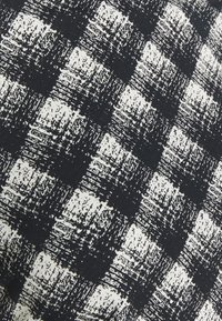 Czarno-biała abstrakcyjna tkanina w kratkę z teksturowanym wzorem, z nierównymi detalami pociągnięć pędzla i ciemnym tłem.