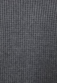 Grauer, gerippter Stoff mit strukturierter Oberfläche, versehen mit vertikalen Linien und einem weichen, flexiblen Erscheinungsbild. Geeignet für Bekleidung oder Accessoires.