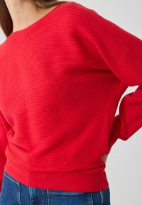 Pull en maille côtelée rouge avec un col large et des manches longues, doté d'un ourlet ajusté. Tissu texturé et coupe décontractée.