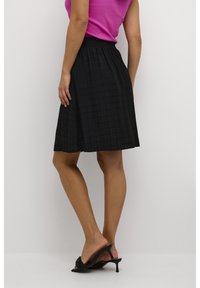 Falda negra hasta la rodilla con un patrón de cuadros texturizado, cinturilla elástica, silueta fluida, combinada con sandalias negras de tacón.