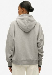 Sudadera gris con capucha, de corte holgado, hombros caídos y puños acanalados. La tela tiene una textura suave y un diseño simple y limpio.