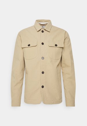 Beżowa koszulowa kurtka z długim rękawem, kołnierzem, zapięciem na guziki z przodu oraz dwoma patkowymi kieszeniami na piersiach z guzikami.