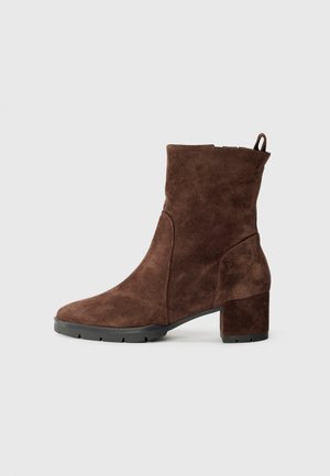 Stivale alla caviglia in suede marrone con tacco a blocco, punta arrotondata, dettaglio delle cuciture laterali e linguetta sul retro. Suola in gomma per una maggiore aderenza.