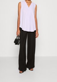 Vaaleanlila ilmanhiha toppi V-pääntiellä, yhdistettynä mustiin leveälahkeisiin housuihin ja pieneen mustaan käsilaukkuun. Pehmeä kangas, yksinkertainen muotoilu.