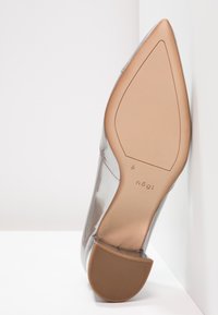 Chaussure transparente à bout pointu avec semelle couleur cognac et talon bloc vue par le dessous, marque "högl", avec matière supérieure transparente.