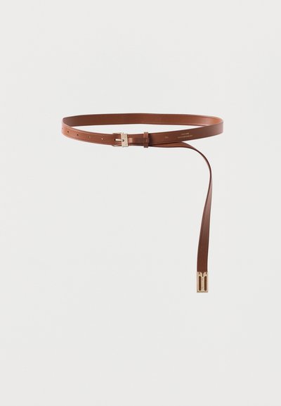 Καφέ δερμάτινη ζώνη με χρυσή αγκράφα, το ένα άκρο κρέμεται ελεύθερα, σε ουδέτερο ανοιχτό φόντο.