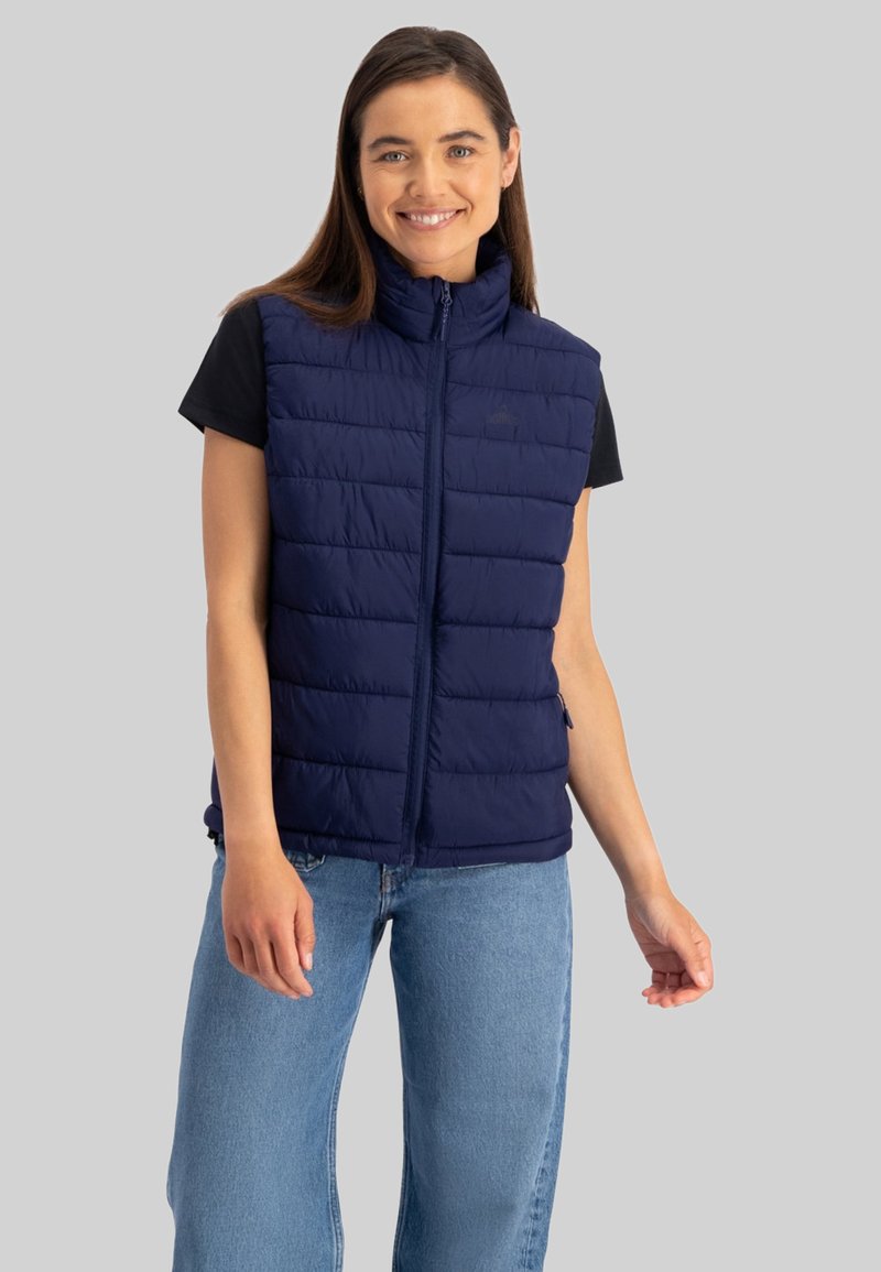 Marine blazervest met hoge kraag, ritssluitingen aan de voorkant en een horizontale quiltpatroon. Gedragen over een zwart t-shirt en gecombineerd met blauwe jeans.