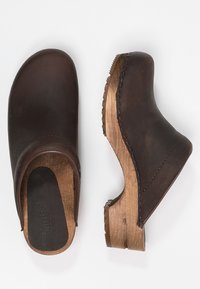 Donkerbruine leren klompen met een houten zool. Kenmerken zijn een ronde neus, een gebogen ontwerp en zichtbare stiksels langs de randen.
