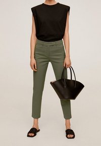 Haut noir sans manches, pantalon ajusté vert olive, sac fourre-tout noir, sandales plates noires. Design simple, textures lisses, palette de couleurs neutres.