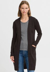 Dark brown long cardigan made of knitted fabric, featuring two front pockets, ribbed cuffs, and an open front design. Worn over a gray top.