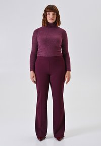 Bordeaux coltrui in een glinsterende brei met bijpassende hoge taille, wijde broek. Zachte textuur; aansluitende silhoeet.