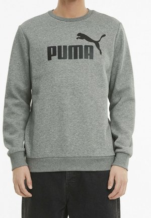 Person iført en grå Puma langærmet sweatshirt med sort logotekst og springende puma-grafik, kombineret med mørke bukser.