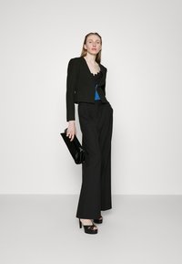 Svart croppet jakke med lange ermer, blå topp med blonder, vide svarte bukser, svart clutch, og høyhælte sandaler.