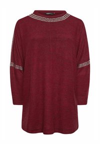 Burgundy topp med bred halsringning, pryds av silverfärgade nitar längs kragen och ärmarna. Tillverkad av mjukt, texturerat tyg. Avslappnad passform.